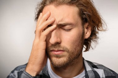 Genç adam ışık arka plan üzerinde baş ağrısı muzdarip