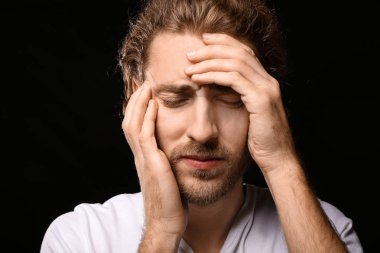Genç adam koyu arka plan üzerinde baş ağrısı muzdarip