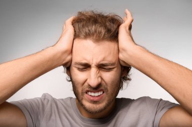 Genç adam ışık arka plan üzerinde baş ağrısı muzdarip