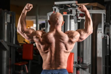 Spor salonunda kaslı bir adam poz veriyor.