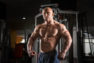 Spor salonunda kaslı bir adam poz veriyor.
