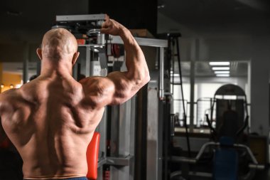 Spor salonunda kaslı bir adam poz veriyor.