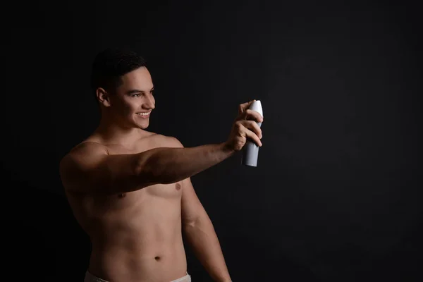 Young man with deodorant on dark background