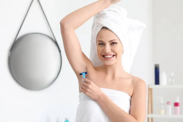 Beautiful young woman shaving armpits in bathroom