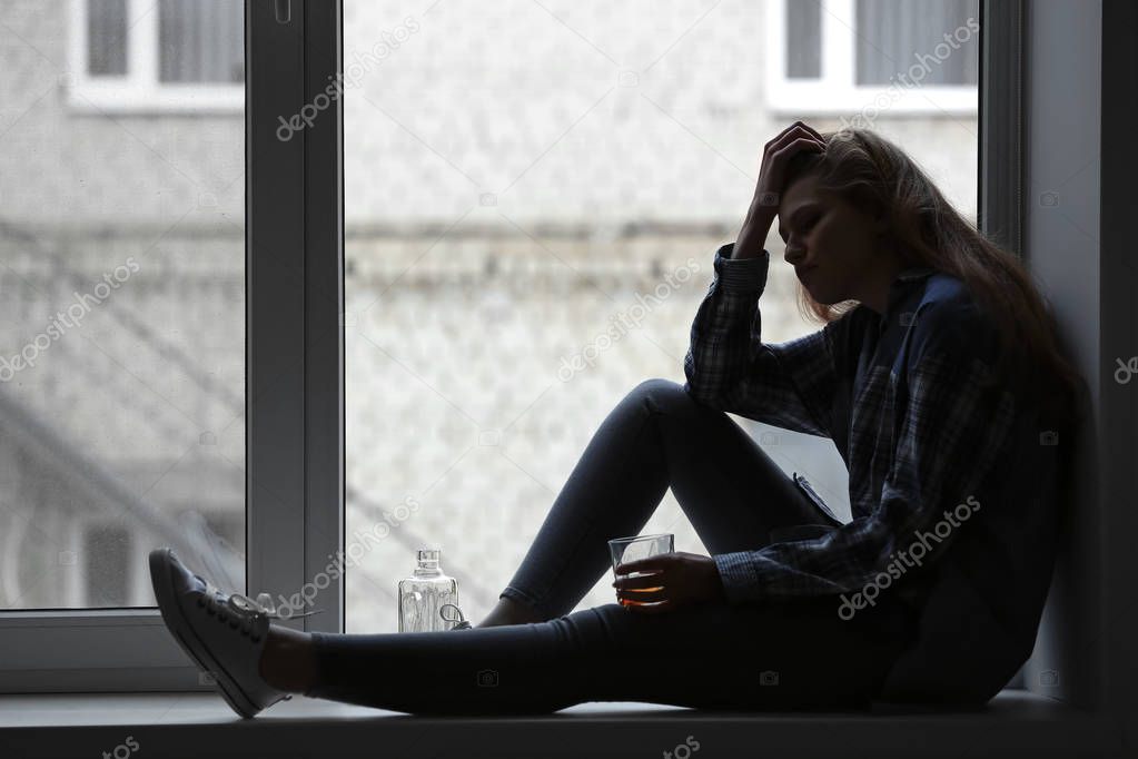 Depressed woman drinking alcohol near window