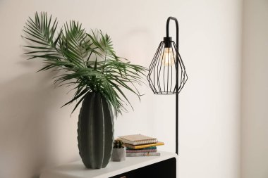 Işık duvarının yakınında tablo vazo ile yeşil tropikal yaprak