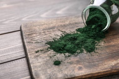 Devrilmiş cam kavanoz ahşap tahta üzerinde spirulina tozu ile