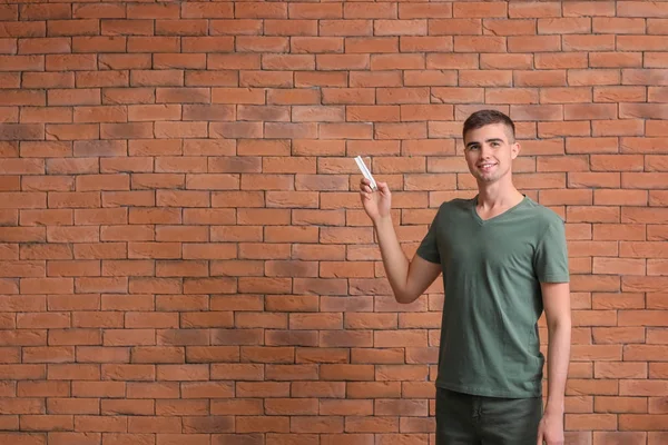 Young man switching on air conditioner against brick background