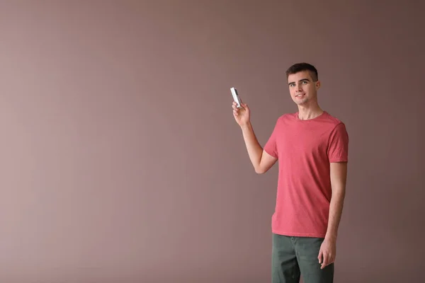 Young man switching on air conditioner against color background