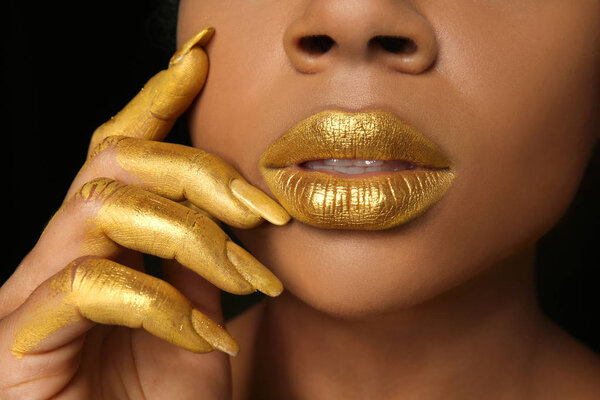 African-American woman with golden paint on her body against black background, closeup