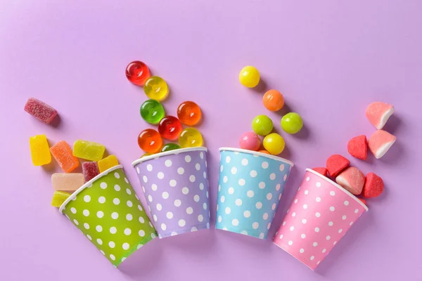 Cups with different tasty candies on color background