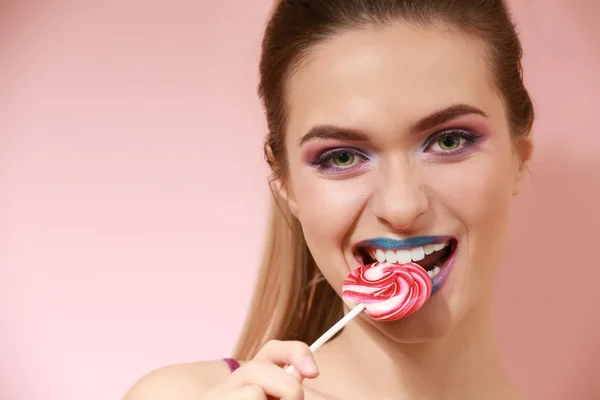 美丽的年轻女子与不寻常的化妆和甜蜜的棒棒糖在颜色背景 — 图库照片