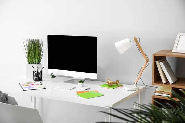 Stylish workplace with modern computer near light wall