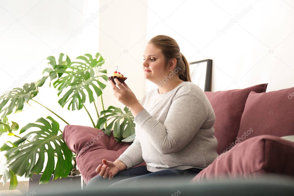 Beautiful plus size girl with sweet cake at home. Concept of body positivity