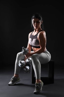 Koyu arka plan üzerinde dumbbells ile sportif kaslı kadın