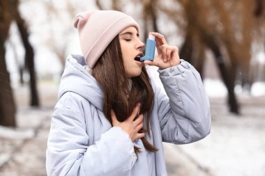 Young woman with inhaler having asthma attack outdoors clipart