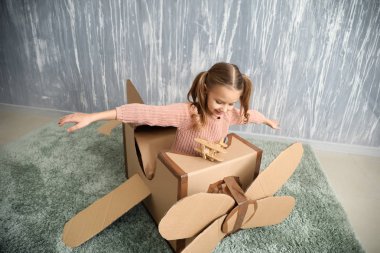 Küçük kız odasında karton uçak ile oynarken