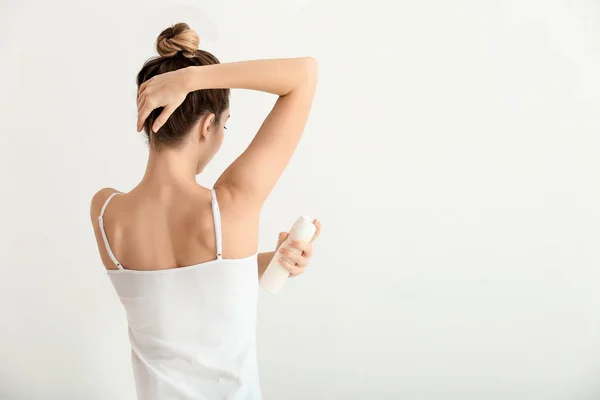 Beautiful young woman with deodorant on light background