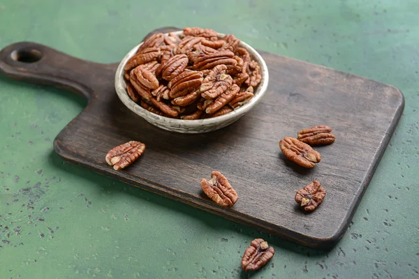 Wooden board with pecan nuts on color background