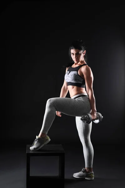 Sporty muscular woman with dumbbell on dark background