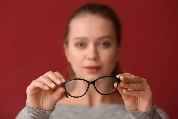 Young woman with bad sight holding eyeglasses on color background