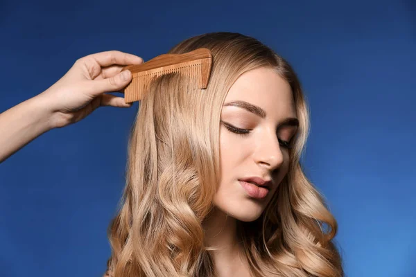 Female hand combing hair of beautiful woman on color background