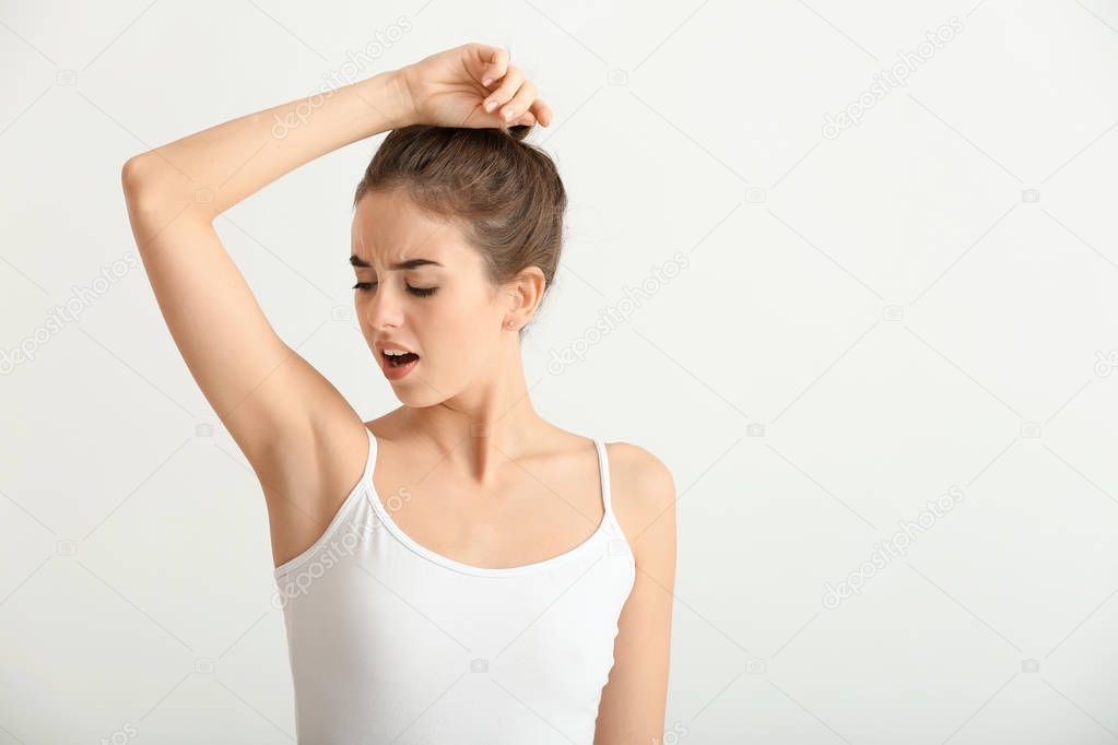 Beautiful young woman feeling smell of sweat on light background. Concept of using deodorant
