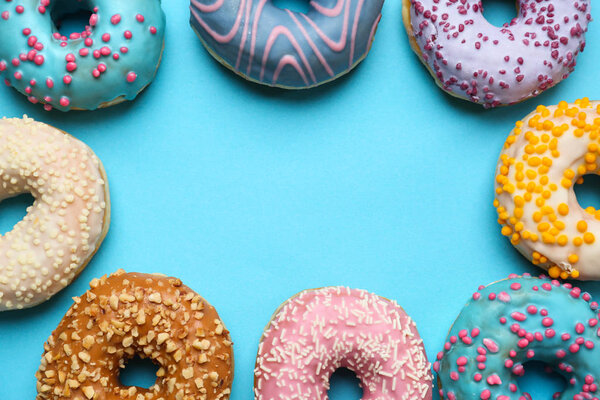 Frame made of sweet tasty donuts on color background