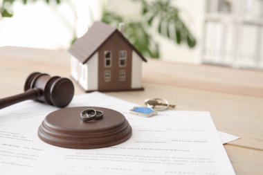Rings with decree of divorce, judge gavel and key from house on table. Concept of dividing marital property clipart