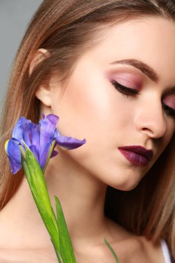 Gri arka planda çiçekleri olan güzel genç bir kadın.