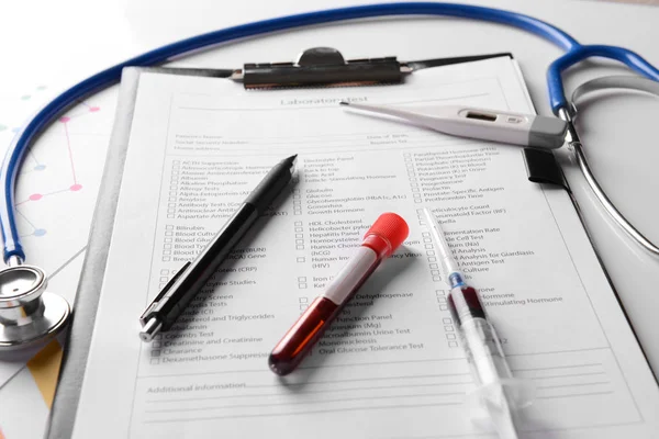 Laboratory test form, thermometer, stethoscope and test-tube with blood on table in clinic