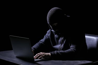 Koyu arka plan üzerine masada oturan dizüstü bilgisayar ile profesyonel hacker