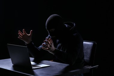 Koyu arka plan üzerine masada oturan dizüstü bilgisayar ile duygusal hacker