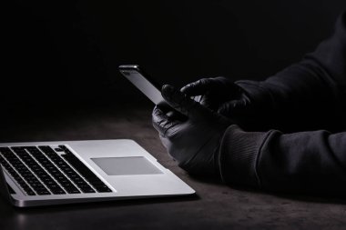 Dizüstü bilgisayar ve cep telefonu koyu arka plan üzerine masada oturan Profesyonel hacker