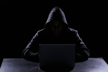 Koyu arka plan üzerine masada oturan dizüstü bilgisayar ile profesyonel hacker