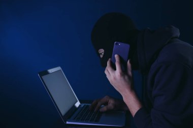 Profesyonel hacker ile cep telefonu koyu arka plan üzerinde dizüstü bilgisayar kullanarak