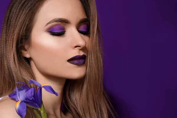 Beautiful young woman with makeup in violet tones and flower on color background