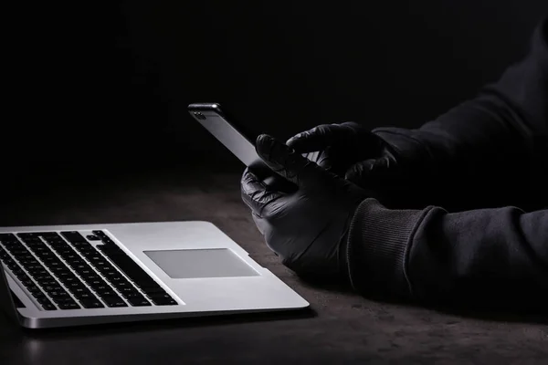 专业黑客与笔记本电脑和手机坐在黑暗的背景的桌子上 — 图库照片