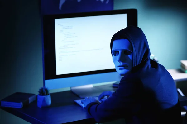 Professional hacker in mask using computer in dark room