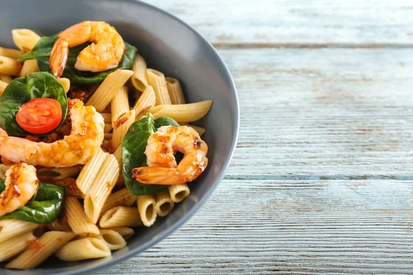 Tasty pasta with shrimps and tomatoes in bowl on wooden table, closeup