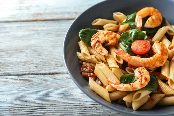 Tasty pasta with shrimps and tomatoes in bowl on wooden table, closeup