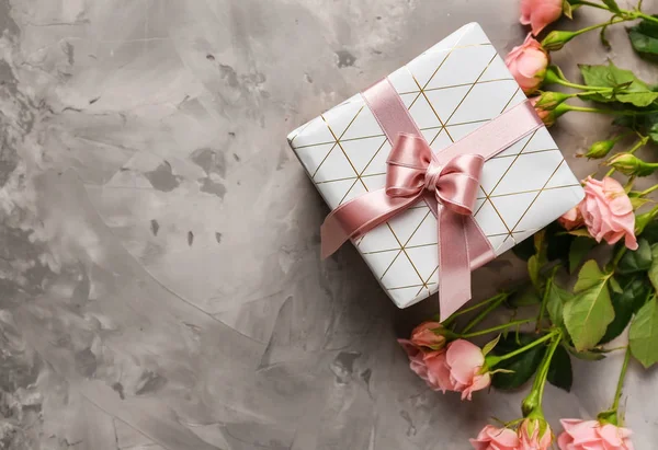 Festive gift box and flowers on grey background
