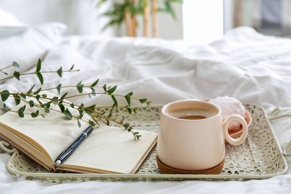 Tray with cup of coffee and notebook on bed