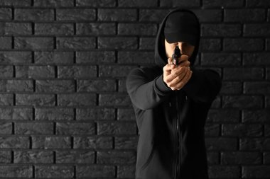 Erkek suçlu Görüntüleyicisi karanlık tuğla arka plan karşı bir silah işaret