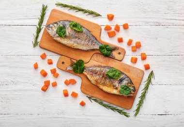 Kurulları ızgara dorado balık, havuç ve beyaz ahşap zemin üzerinde otlar ile