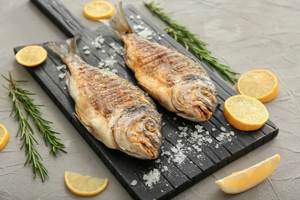 Board with grilled dorado fish and lemon on grey background