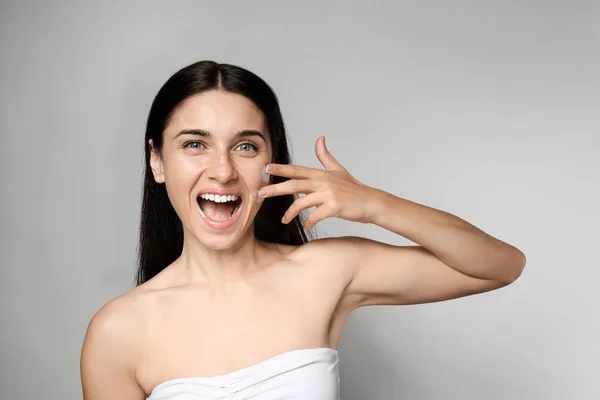 Retrato Una Hermosa Mujer Joven Aplicando Crema Facial Sobre Fondo — Foto de Stock