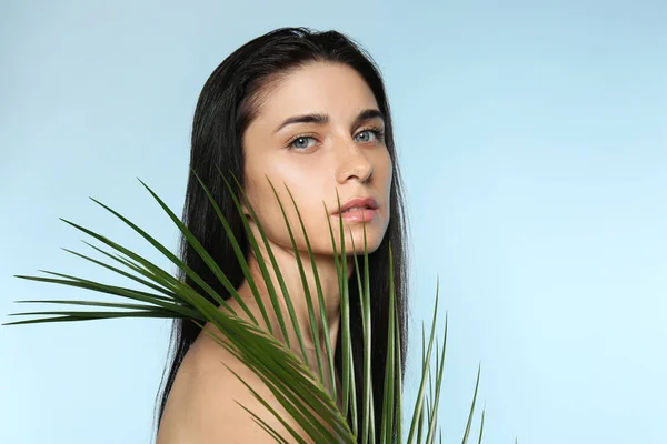 Portrait of beautiful young woman with natural makeup and tropical leaf on color background