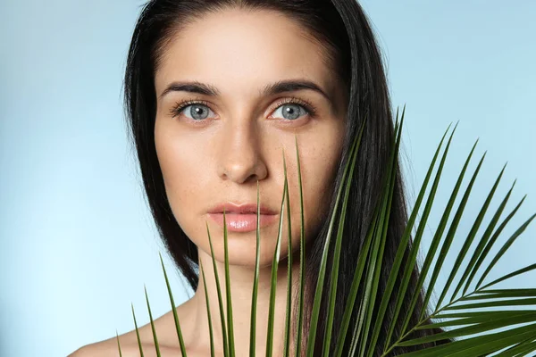 Portrait of beautiful young woman with natural makeup and tropical leaf on color background