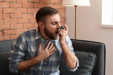 Astım spreyi olan genç bir adam evde astım krizi geçiriyor.
